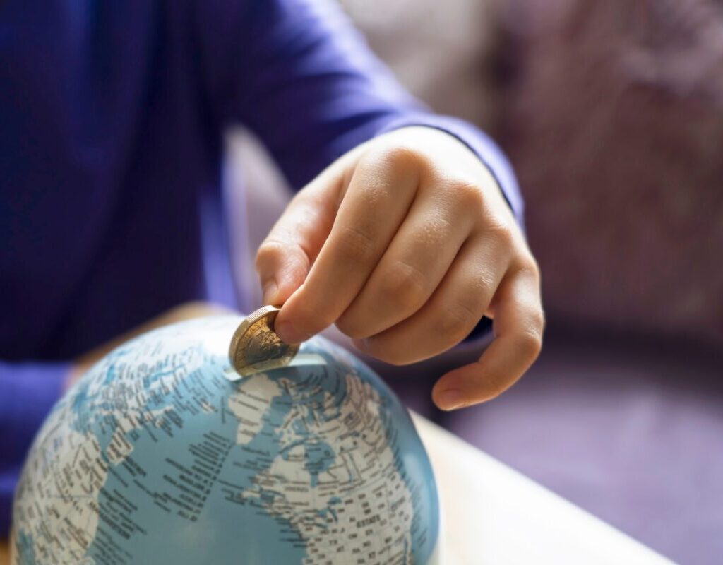 kid hand putting one pound coin into piggybank to donate money helping the earth